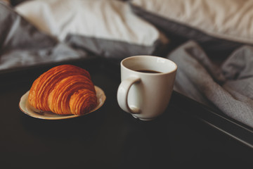 Breakfast on a tray in bed at home white dark linen. croissant tea strawberries.