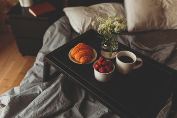Breakfast on a tray in bed at home white dark linen. croissant tea strawberries.