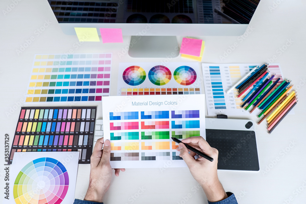 Poster Image of male creative graphic designer working on color selection and drawing on graphics tablet at workplace with work tools and accessories, top view workspace