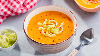 Hot pumpkin or carrot cream soup with spices on concrete background. Closeup of autumn spicy soup, healthy eating, top view