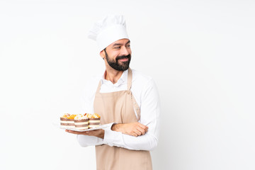 Young man holding muffin cake over isolated white background with arms crossed and happy