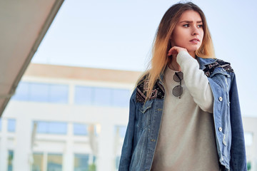 Fototapeta premium beautiful charismatic girl in a light sweatshirt v denim jacket with long blonde hair on a summer day