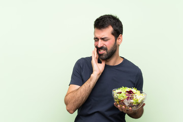 Young handsome man with salad over isolated green wall with toothache