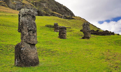 Four moai statues against a blue sky with clouds and green grass field in the Rano Raraku Volcano...