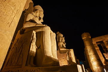 Statue and hieroglyphic carvings at an ancient egyptian temple in night