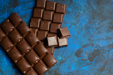 bar of dark chocolate on a blue background with sprinkled cocoa