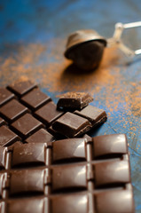 bar of dark chocolate on a blue background with sprinkled cocoa