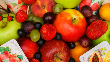 Set of berries and fruits in wooden box. Apple, strawberry, grape, berry and peach on a red brick...