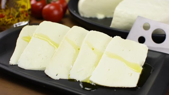 Pouring olive oil in slices of buffalo fresh cheese made in Serra da Canastra, in a platter in wood background