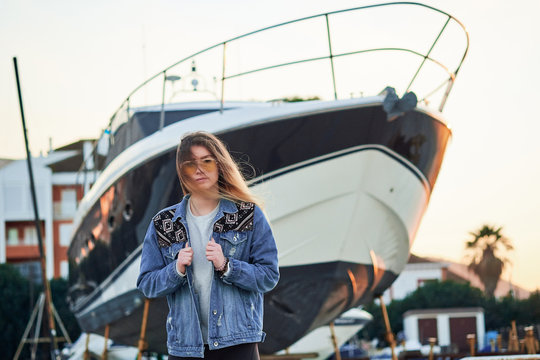 beautiful girl in sunglasses and a denim jacket with long blonde hair in a summer sunset on the background of a large luxurious yacht