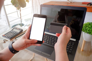 Cropped shot view of woman or man hands holding credit card, typing on laptop computer keyboard for internet banking and payment with phone. Online shopping.