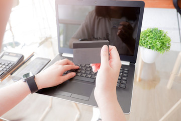 Cropped shot view of woman or man hands holding credit card, typing on laptop computer keyboard for internet banking and payment with phone. Online shopping.