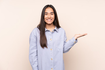 Young Indian woman isolated on beige background holding copyspace imaginary on the palm to insert...