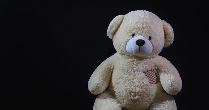 A lively toy bear looking at the camera and nodding hid head or dancing on a black studio background with dramatic light and free space for inscription.