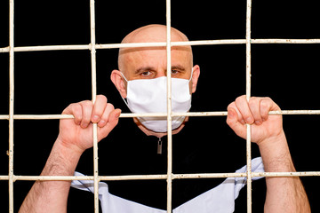 pandemic containment and quarantine concept the middle-aged bald man in a medical hygiene mask holding iron bars with his hands - obrazy, fototapety, plakaty
