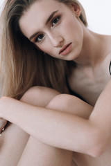 Blonde in a black swimsuit with long hair posing in the studio on a white background. Dressed in a white jacket and a straw hat