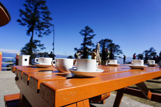 An outdoor cafe table at Changla Pass in Bhutan having a couple of white tea cups kept in the background of deep blue sky and trees. 