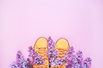 Orange sneakers and a bouquet of lilac on a pink background, copy space, top view. Romantic background