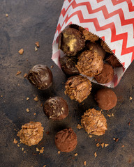 Chocolate truffle bonbon with waffle crumbs and cocoa powder in a paper bag on a dark background