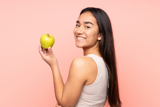 Young Indian woman isolated on pink background eating an apple