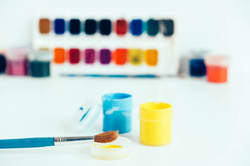 Colorful gouache paints and brush for painting on white wooden table. Copy, empty space for text