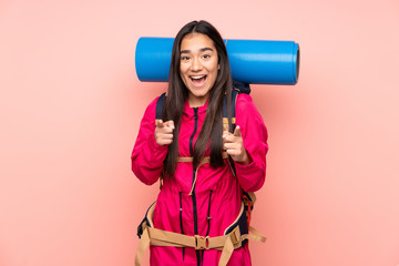 Young mountaineer Indian girl with a big backpack isolated on pink background points finger at you