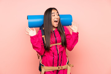 Young mountaineer Indian girl with a big backpack isolated on pink background with surprise facial expression