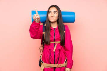 Young mountaineer Indian girl with a big backpack isolated on pink background touching on transparent screen