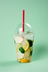 Lemonade to go cup with mint, lime and lemon on lightgreen background, isolated