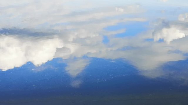 Clouds on a blue sky with reflection on the surface of the water in the lake.