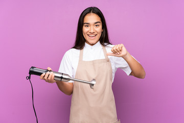 Indian woman using hand blender isolated on purple background proud and self-satisfied