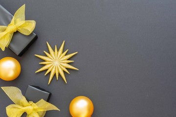Festive background with gold decorations , shiny golden star and gift boxes and christmas balls on a black background , flat lay, top view, copy space