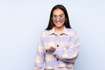 Young Indian woman isolated on blue background presenting an idea while looking smiling towards