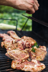 Meat steaks are grilled on an outdoor street grill. Man cooks barbecue and adds spices. Summer picnic in nature.