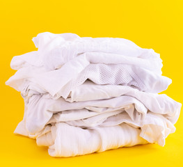 White summer light clothing on a yellow background, a stack of casual clothes isolated