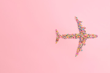 Creative travel concept in candy minimal style. Airplane made of colorful sugar sprinkles on pastel pink background. Top view flat lay image with copy space.
