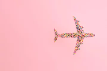 Tuinposter Creative travel concept in candy minimal style. Airplane made of colorful sugar sprinkles on pastel pink background. Top view flat lay image with copy space. © loominatis