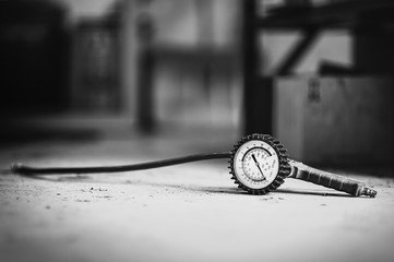 Analog tire pressure gauge with a hose lying on the ground of a car repair shop (black and white version of photo).