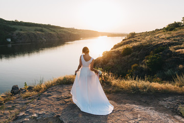 Fototapeta na wymiar Bride in a luxurious white wedding dress in nature at sunset