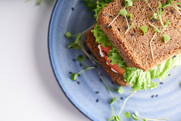 healthy sandwich with gluten-free bread, tomato, lettuce and germinated microgreens, sprinkled with sesame seeds served in plate