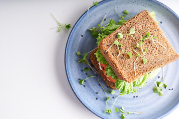 healthy sandwich with gluten-free bread, tomato, lettuce and germinated microgreens, sprinkled with sesame seeds served in plate