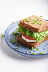 healthy sandwich with gluten-free bread, tomato, lettuce and germinated microgreens, sprinkled with sesame seeds served in plate