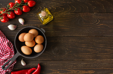 Empty pan on brown wooden background, fresh juicy tomatoes with garlic and red pepper, olive oil in a bottle and eggs, breakfast , top view, copy spaceingredients