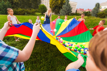 Kids holding rainbow parachute with colorful balls on it