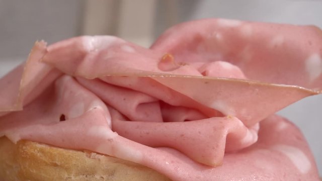 Preparation of a sandwich with mortadella, close-up view, hands working with bread and salami.