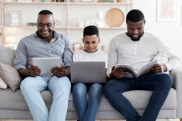 Three Generations Of Men With Digital Tablet, Laptop And Magazine At Home