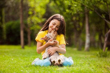 The happy girl is hugging her yorkshire terrier in the garden