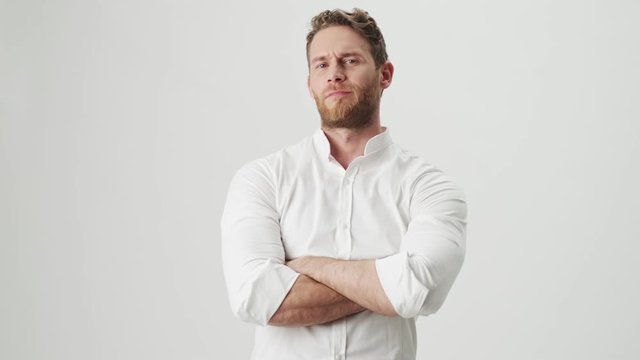 Handsome young displeased man in white shirt isolated over white wall background showing thumbs down