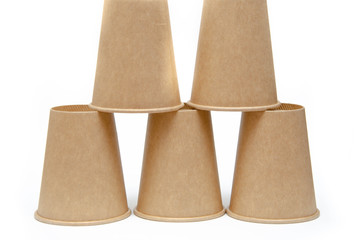 Brown paper cup for coffee, tea, a drink from environmental materials on a white background. The male hand builds a pyramid of cups in macro and overall plan. Place for text on the left and right.