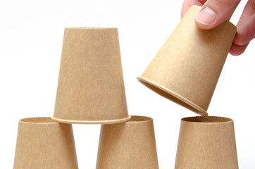 Brown paper cup for coffee, tea, a drink from environmental materials on a white background. The male hand builds a pyramid of cups in macro and overall plan. Place for text on the left and right.